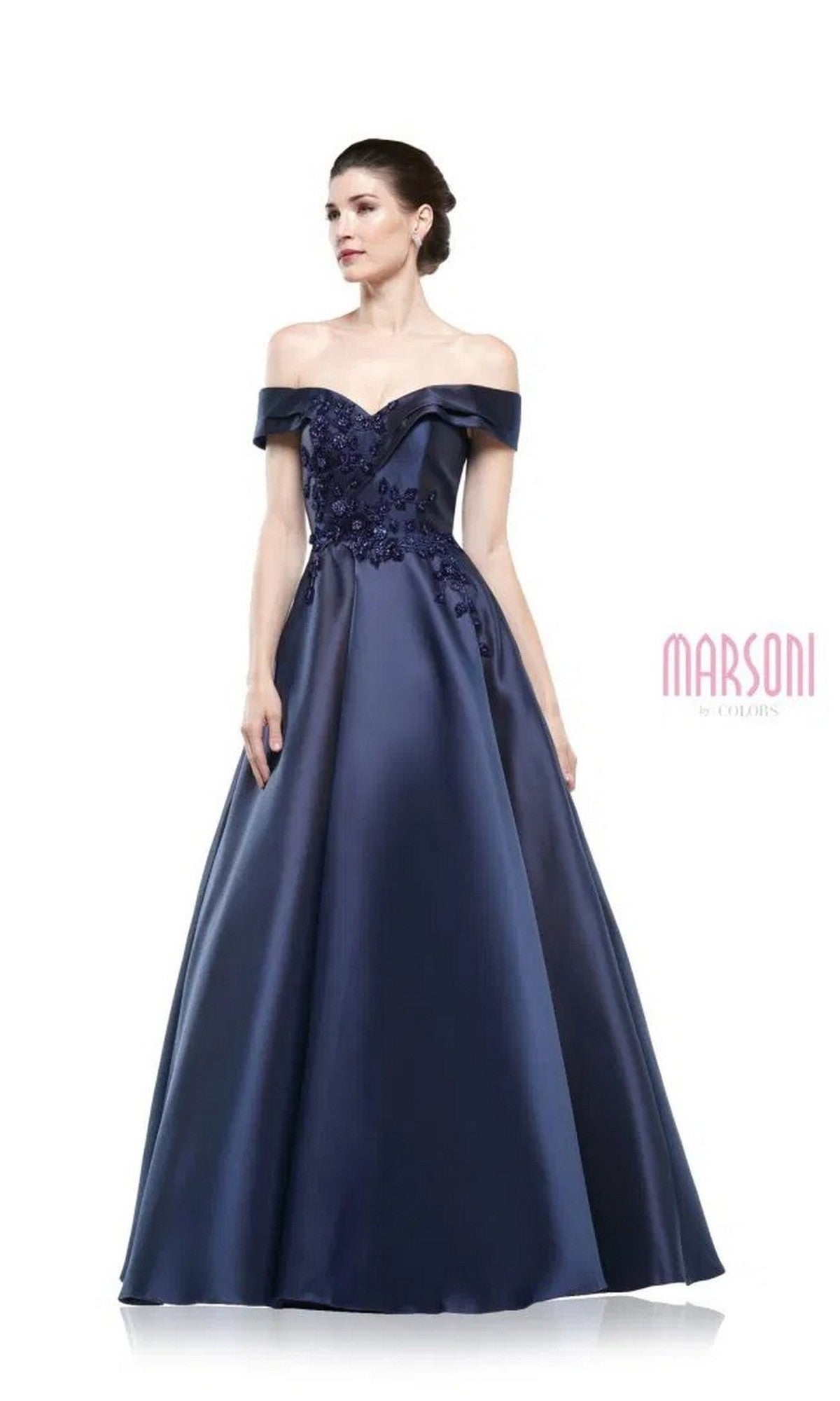 A woman wears the Marsoni MV1008 long formal dress in navy, featuring an off-the-shoulder design and floral embroidery on the bodice, standing against a plain white background.